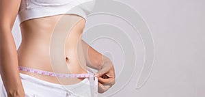 Close up slim young woman measuring her thin waist with a tape measure. Healthcare and woman diet lifestyle concept to reduce