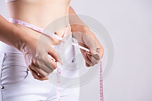 Close up slim young woman measuring her thin waist with a tape measure. Healthcare and woman diet lifestyle concept to reduce