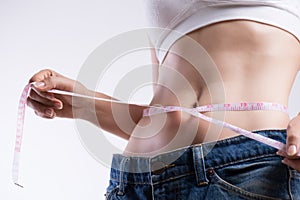 Close up slim young woman measuring her thin waist with a tape measure. Healthcare and woman diet lifestyle concept to reduce