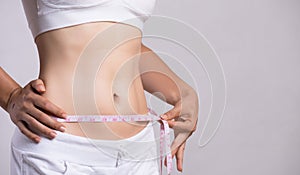 Close up slim young woman measuring her thin waist with a tape measure. Healthcare and woman diet lifestyle concept to reduce