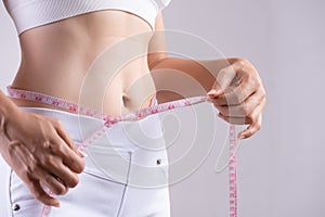 Close up slim young woman measuring her thin waist with a tape measure. Healthcare and woman diet lifestyle concept to reduce