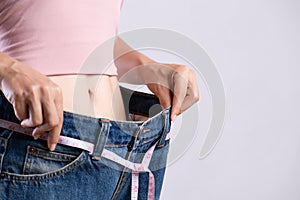 Close up slim young woman measuring her thin waist with a tape measure. Healthcare and woman diet lifestyle concept to reduce