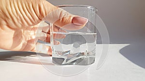 Close-up of a slow hand rotation of a clear glass of cold water on a white background