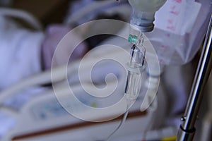 close up of a slow intravenous drip with a blurred lit neon in the background in a hospital room