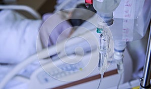 close up of a slow intravenous drip with a blurred lit neon in the background in a hospital room