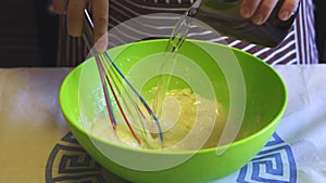 Close-up slow motion of a female hand adds water to flour in a green bowl in the home kitchen. Cooking pancakes