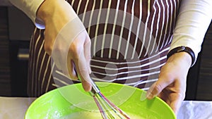 Close-up slow motion of a female hand mixes a batter with a kitchen whisk in a green bowl in the home kitchen. Cooking