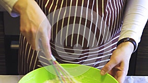 Close-up slow motion of a female hand mixes a batter with a kitchen whisk in a green bowl in the home kitchen. Cooking