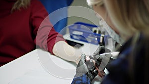 A close up slow motion filming of a client in a red coat undergoing an operation of shape and polish manicure in a spa