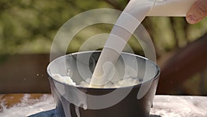 Close-up in slow motion of fresh milk pouring into a bowl in a summer kitchen on a sunny day.