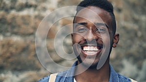 Close-up slow motion portrait of African American male with expressive face smiling showing teeth and looking at camera