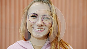 Close-up slow motion portrait of beautiful young blonde wearing glasses smiling outdoors