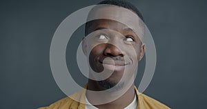 Close-up slow motion portrait of playful African American man rolling eyes making funny face on grey background