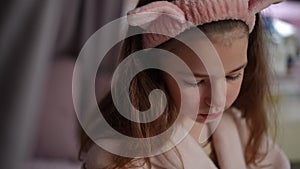 Close-up. Slow motion. A pretty girl with long hair sits in the bedroom on a bed in a bathrobe with a pink hair band on