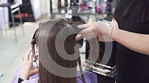 A close-up of a slow-motion shot from the back of the keratin hair straightening procedure, the hairdresser separates