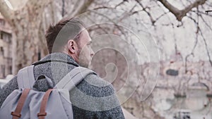 Close-up slow motion shot of confident Caucasian businessman with backpack walking along Tiber river bank on vacation.