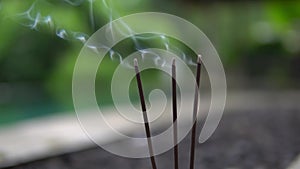 Close up and slow motion of three burning incense sticks outdoors, appeasement