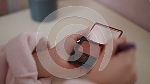 Close-up. Slow motion. An unrecognizable girl holds an open powder compact with a small mirror in her hand and carefully