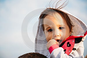 Close up of small baby girl in grey hood sitting on father`s shoulders on the sky background