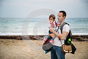 Close up of small baby girl in sweatshirt in father`s hands on the sea coast