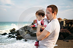 Close up of small baby girl in sweatshirt in father`s hands on the sea coast