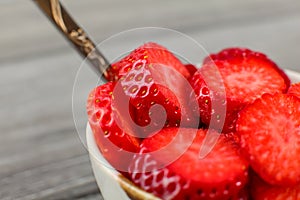 Close up - small bowl with spoon, full of strawberries cut into