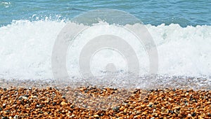 Close-up of small brown wet pebbles on the beach, white wave foam and a blue water. Short depth of focus.