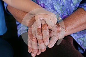 Close-up of small child hand holdiing on elderly person`s hand grandmother with Alzheimer and Parkinson disease. Concepts of