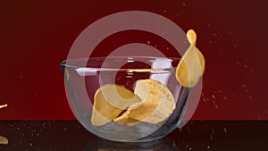 Close up of a small glass bowl and many potato chips falling into it and on the dark table. Stock footage. Spicy