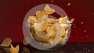 Close up of a small glass bowl and many potato chips falling into it and on the dark table. Stock footage. Spicy