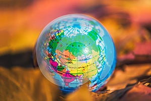 Close up of a small globe lies on colorful autumn maple leaves in the autumn forest. Concept. Selective focus. Russia, Europe