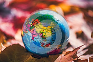 Close up of a small globe lies on colorful autumn maple leaves in the autumn forest. Concept. Selective focus. Russia, Europe