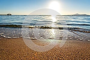 Close up of small sea waves with clear blue water over yellow sand beach at summer sunny shore