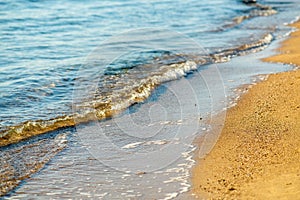 Close up of small sea waves with clear blue water over yellow sand beach at summer sunny shore