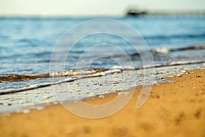Close up of small sea waves with clear blue water over yellow sand beach at summer sunny shore