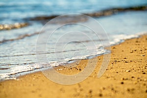Close up of small sea waves with clear blue water over yellow sand beach at summer sunny shore