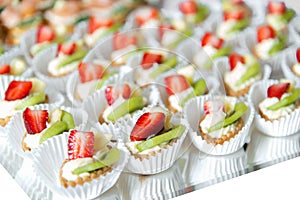 Close up of small sweet canapes arranged on a mirror plate over light background