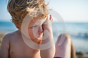 A close-up of small toddler boy on beach on summer holiday. Copy space.