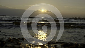 Close-up of small waves on background of sunset. Creative. Rolling small waves on seashore with sunset horizon. Waves on