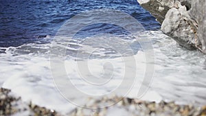Close-up of small waves on sandy beach with rocks. Art. Beautiful blue waves break with white foam on sandy shore and