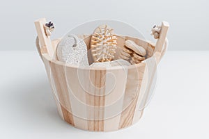 Close-up of small wooden bucket with some bath accessories; hairbrush, washcloth, pumice stone and massager tool.