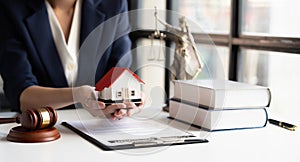 Close-up of and small wooden toy house on table with female lawyer on background and.holding that wooden toy house