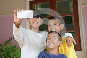 Close up of smartphone and a group of Asian boys taking group selfies against the background of outdoors and a green forest. Three
