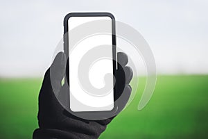 Close-up of smartphone with mockup in male hand dressed in black glove, on background of white and green background.