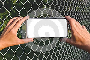 Close-up. Smartphone mockup in woman& x27;s hands. Against the background of a steel wire fence and nature