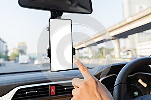 Close-up smartphone with white mockup on screen, background of car steering wheel. A person is pointing at a phone mounted on the