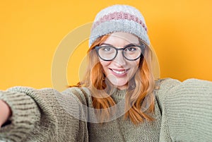 Close-up smile woman takes photo of himself with her smartphone. Selfie, isolated on yellow background. Focus on face