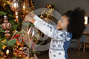Close up smiling African American girl hanging baubles, decorating tree