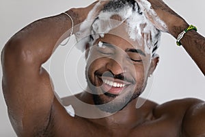 Close up smiling African American man washing hair with shampoo