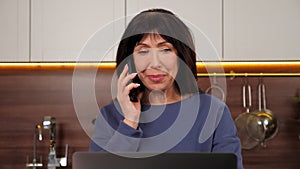 Close up smiling aged woman talking on mobile phone with family in home kitchen